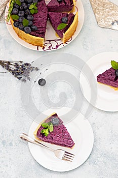 Piece of blueberry or bilberry cheesecake decorated with fresh berries, mint and rosemary. Light grey background. Selective focus