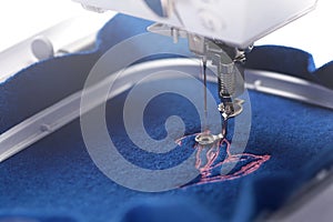 A piece of boiled wool fabric in vivid trendy blue color is being equipped with a magnolia embroidery in light pink