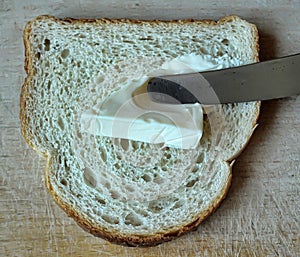 A piece of bread and a knife with cream cheese