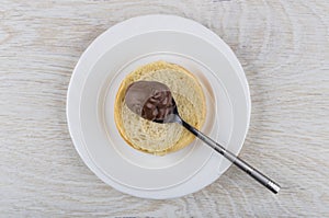 Piece of bread, teaspoon with nut-chocolate paste in plate