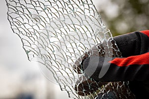 A piece of broken toughened glass held in a hand in a rubber worker glove