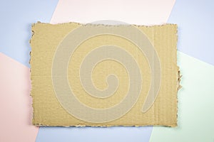 Piece of brown corrugated cardboard on colorful background. Ripped kraft carton paper card. Cardboard torn edge. Top