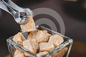 A piece of brown sugar is pulled from a vase with sugar with the help of pastry tweezers.