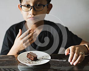 A piece of brownie on the small plate with young boy wearing glasses in the background