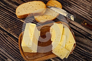 A piece of butter and slices of cheese in a wooden butter dish, fresh wheat toast and a knife with a wooden handle on a wooden