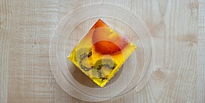 A piece of cake with kiwi and strawberries in jelly on a glass saucer.