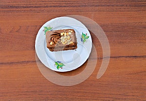 Piece of cake with nuts on plate on wooden table. Top view