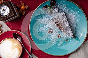 Piece of carrot cake, covered with powdered sugar in a blue plate on a red napkin with cup of coffe and brown sugar