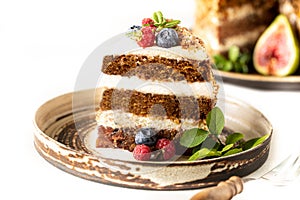 A piece of carrot cake decorated with berries and figs on a white plate. Traditional donkey pastries