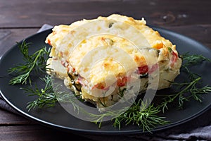 Piece casserole on a plate of potatoes and vegetables with cheese. Dark wooden background. Close up.