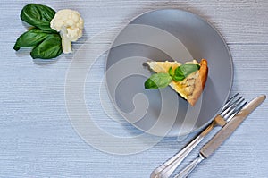 A piece of cauliflower pie on the gray plate decorated with fresh basil leaves, silver knife and fork. Vegetarian cauliflower tart
