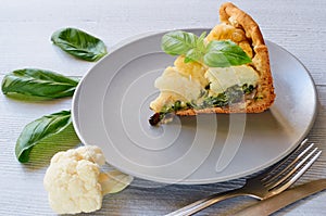 A piece of cauliflower pie on the gray plate decorated with fresh basil leaves and vintage silver knife and fork