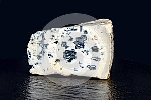 A piece of cheese with blue mould on a black background closeup