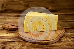 Piece of cheese on cutting board on wooden table