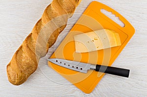 Piece of cheese, knife on cutting board, loaf of bread