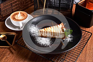 Piece of Cheesecake on black plate on a table with mint and a cup of coffee. Side view