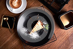 Piece of Cheesecake on black plate on a table with mint and a cup of coffee. Side view
