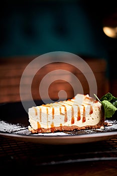Piece of Cheesecake on black plate on a table with mint and a cup of coffee. Side view