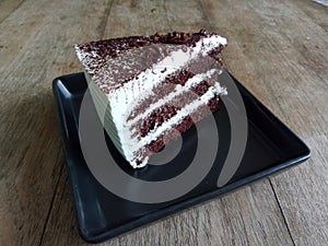 Piece of chocolate cake in black plate on wooden table in coffee shop.