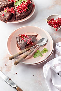A piece of chocolate cake brownie decorated with red currant berries and mint on white marble table