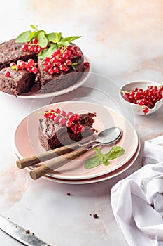 A piece of chocolate cake brownie decorated with red currant berries and mint on white marble table