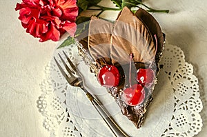 Piece of chocolate cake with cherries and flower China rose on white napkin