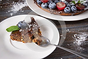 Piece of chocolate cake with fresh blueberries and mint on a white saucer on a dark wooden , dessert