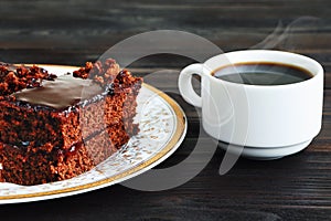 A piece of Chocolate cake on a plate and cup of black coffee on a wooden background.Slice of Homemade brownie cake.Copy