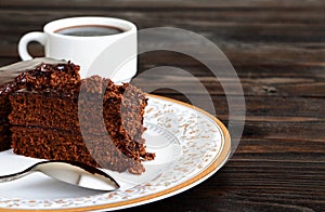 A piece of Chocolate cake on a plate and cup of black coffee on a wooden background.Slice of Homemade brownie cake.Copy