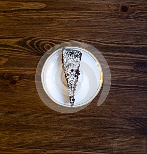A piece of chocolate cake sprinkled with coconut flakes on a white porcelain saucer on a wooden table