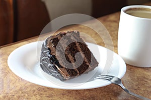 Piece of chocolate cake on a white plate close-up. next to a fork and a cup of coffee. horizontal