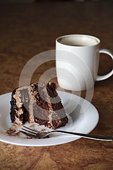 Piece of chocolate cake on a white plate close-up. Verticalnext to a fork and a cup of coffee