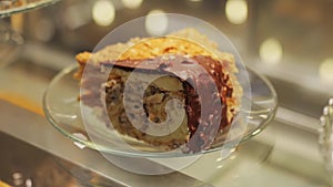 A piece of chocolate nut cake with nougat on a plate in a pastry shop window, close-up. Slow motion