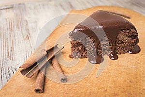 A piece of chocolate pie, cinnamon sticks on a wooden background