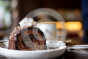 A piece of chocolate roll cake and whipped cream on the top in white ceramics plate and coffee cup on wooden table