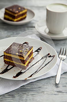 Piece of chocolate three-layer cake on a white plate in a cafe