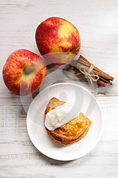 Piece of cinnamon apple pie on a white plate with fresh apple in background, autumn food concept