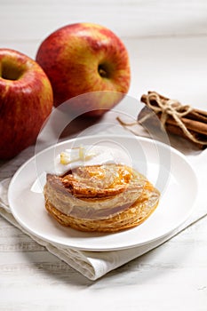 Piece of cinnamon apple pie on a white plate with fresh apple in background, autumn food concept