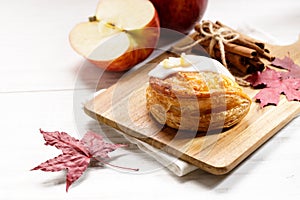 Piece of cinnamon apple pie on a wooden board with fresh apple in background, autumn food concept