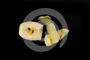 Piece of cut and peeled apple, peels and seeds, on black background