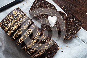 A piece of dark bread with a heart of butter next to sliced bread and a knife on a napkin