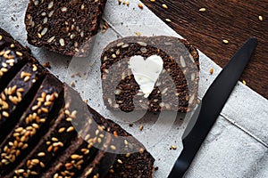 A piece of dark bread with a heart of butter next to sliced bread and a knife on a napkin