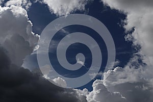 A piece of deep blue summer sky surrounded with white cumulus clouds.