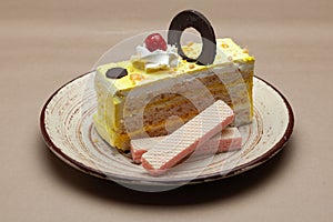A piece of Delicious Butterscotch pastry with a cherry and choclate wafer on top.