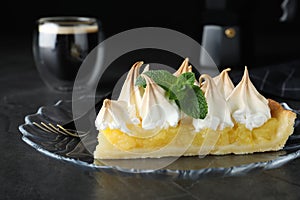 Piece of delicious lemon meringue pie with mint served on black table, closeup