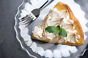 Piece of delicious lemon meringue pie with mint served on black table, top view