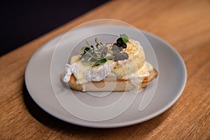 Piece of eggs benedict with delicious garnish on wooden table at restaurant for brunch