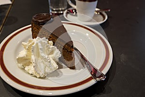 Piece of famous Sachertorte chocolate cake with apricot jam of Austrian origin served with whipped cream