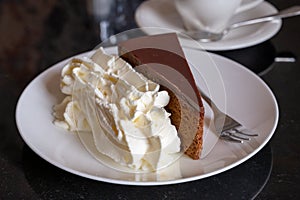 Piece of famous Sachertorte chocolate cake with apricot jam of Austrian origin served with whipped cream