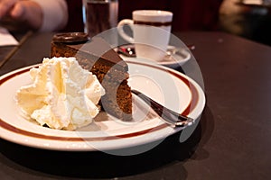 Piece of famous Sachertorte chocolate cake with apricot jam of Austrian origin served with whipped cream